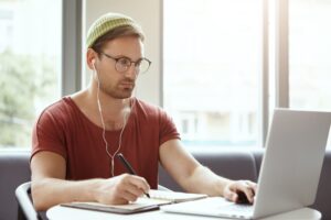 Aluno em uma mesa, em frente ao seu computador, usando fones de ouvido para ouvir seu professor